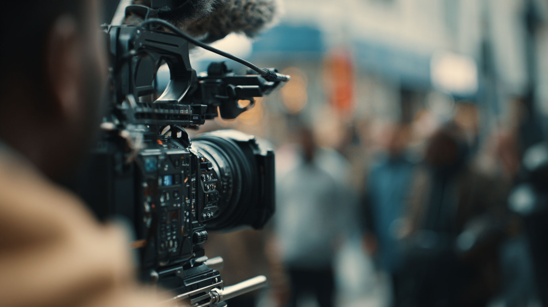 Close-up of a professional video camera on a rig, filming in a busy street.